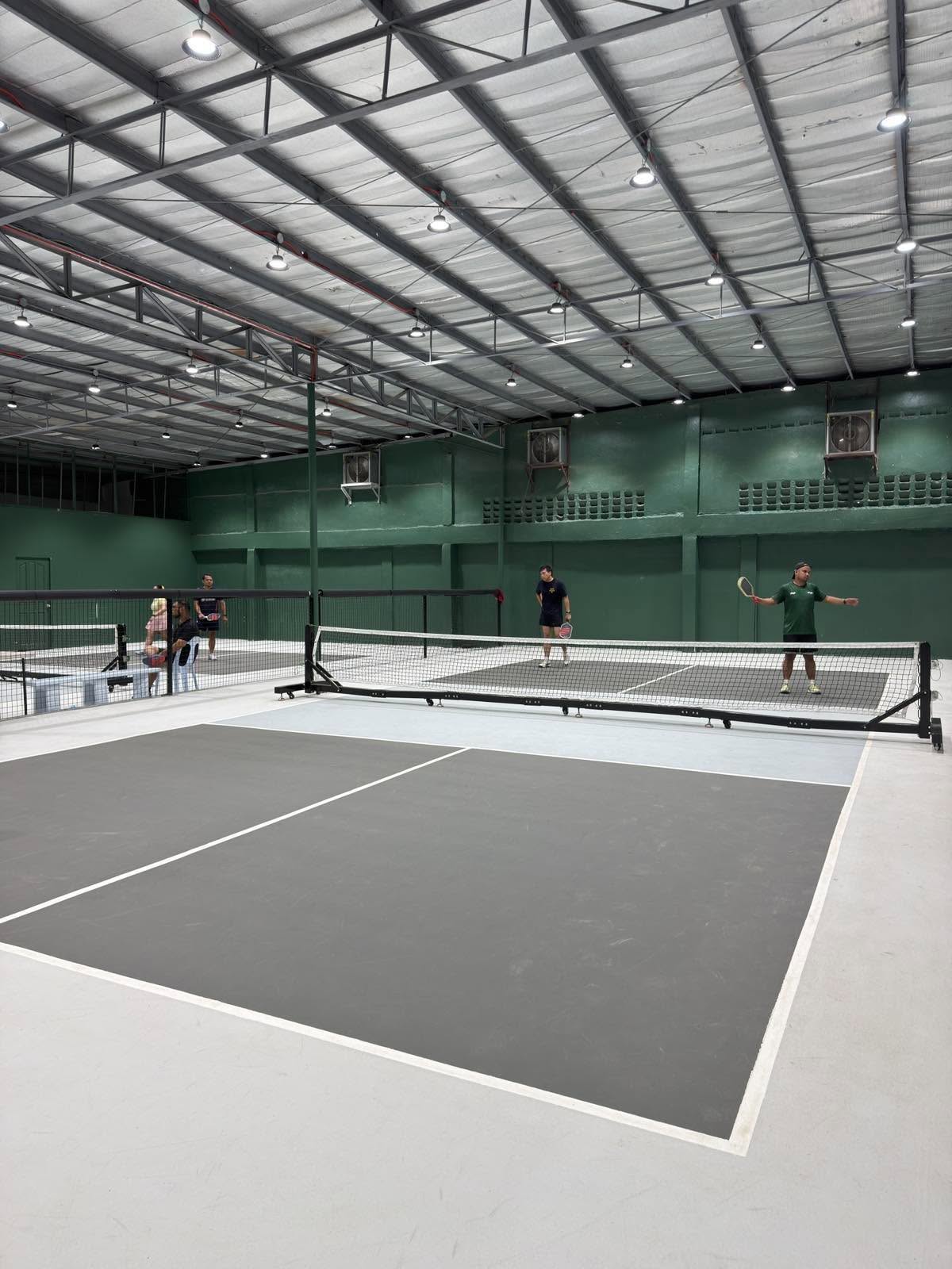 An indoor pickleball court seen from the baseline under high-bay lights