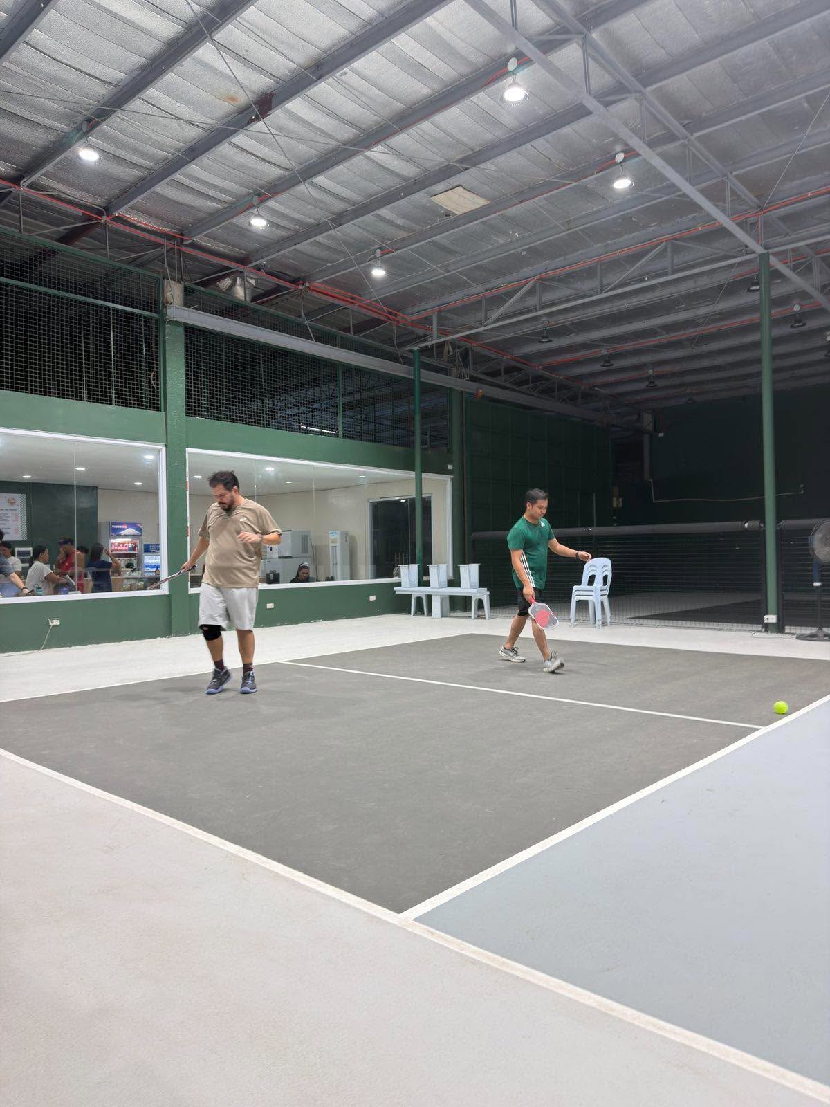 Two pickleball players on court in front of the front desk and café window